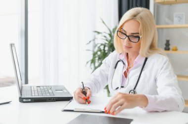 Orta yaşlı kadın doktor portresi boynunda steteskop olan beyaz bir doktor önlüğü giyiyor. Özel klinikte gülümseyen bir doktor..