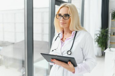 Orta yaşlı kadın doktor portresi boynunda steteskop olan beyaz bir doktor önlüğü giyiyor. Özel klinikte gülümseyen bir doktor..