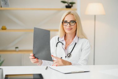 Orta yaşlı kadın doktorun portre fotoğrafı. Masada oturuyor ve doktor ofisinde çalışıyor..