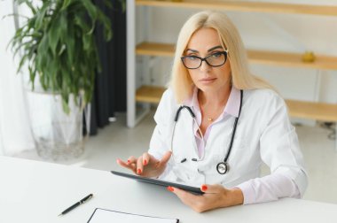 Orta yaşlı kadın doktorun portre fotoğrafı. Masada oturuyor ve doktor ofisinde çalışıyor..