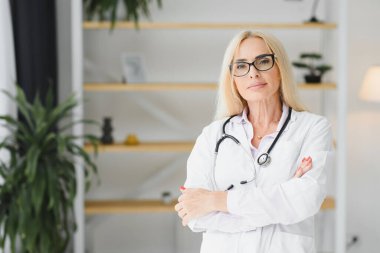 Orta yaşlı kadın doktor portresi boynunda steteskop olan beyaz bir doktor önlüğü giyiyor. Özel klinikte gülümseyen bir doktor..