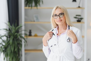Orta yaşlı kadın doktor portresi boynunda steteskop olan beyaz bir doktor önlüğü giyiyor. Özel klinikte gülümseyen bir doktor..