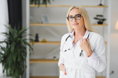 Laboratuvar önlüğü ve steteskop giyen kadın doktor hastanede dikilirken elinde pano tutuyormuş.