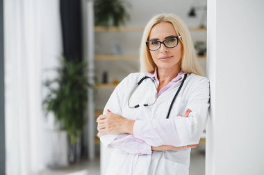 Orta yaşlı kadın doktor portresi boynunda steteskop olan beyaz bir doktor önlüğü giyiyor. Özel klinikte gülümseyen bir doktor..