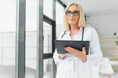 Laboratuvar önlüğü ve steteskop giyen kadın doktor hastanede dikilirken elinde pano tutuyormuş.