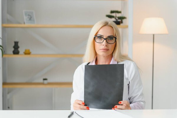 Portrait shot of middle aged female doctor sitting at desk and working in doctor office.