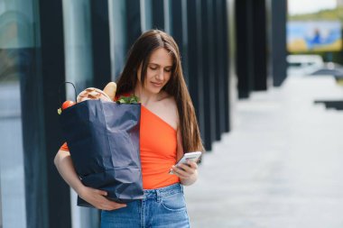 Marketin yanında duran genç kadın elinde bir paket yiyecekle.