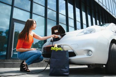 Elektrikli benzin istasyonunda kadın elektro arabayı şarj ediyor..