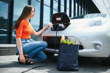 Eko elektrikli araba konsepti. Elektrikli arabanın şarj olmasını bekleyen kadın.