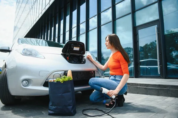 Eko elektrikli araba konsepti. Elektrikli arabanın şarj olmasını bekleyen kadın.