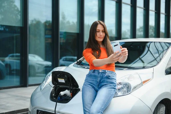 Beklerken Akıllı Telefon Kullanmak Elektrikli Arabalardaki Kadın Gündüz Şarj Istasyonunda — Stok fotoğraf