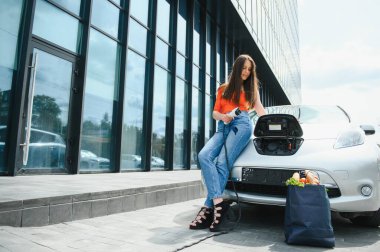 Eko elektrikli araba konsepti. Elektrikli arabanın şarj olmasını bekleyen kadın.