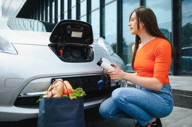 Eko elektrikli araba konsepti. Elektrikli arabanın şarj olmasını bekleyen kadın.