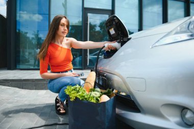 Elektrikli benzin istasyonunda kadın elektro arabayı şarj ediyor..