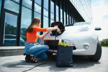 Kadın elektrik istasyonunda elektro arabayı şarj ediyor..