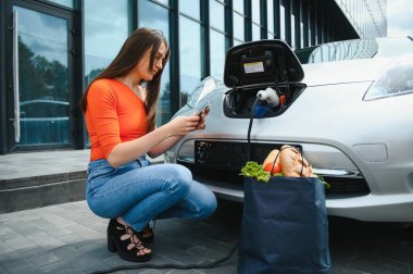 Elektrikli benzin istasyonunda kadın elektro arabayı şarj ediyor..