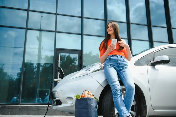 Young Woman Standing Electric Car Looks Smart Phone Rental Car — Stock Photo, Image