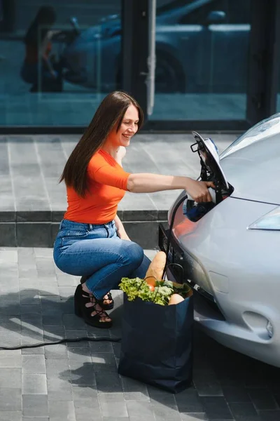 Elektrikli benzin istasyonunda kadın elektro arabayı şarj ediyor..