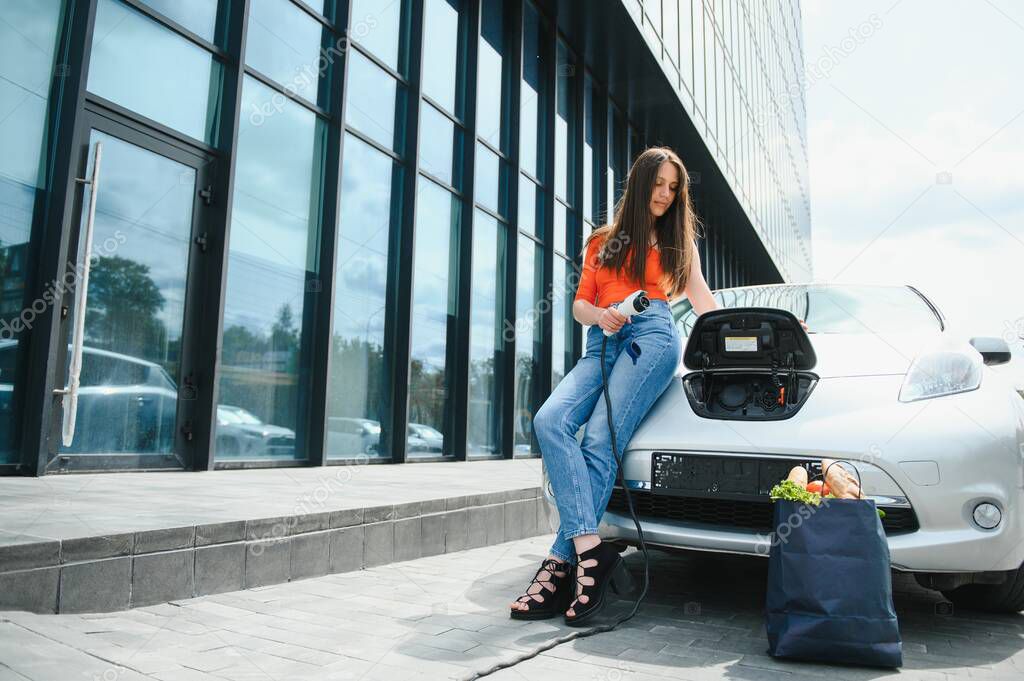 Eco electric car concept. Woman waiting electric car to charge
