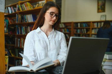 Üniversite Kütüphanesi: Güzel Akıllı Kafkasyalı Kız dizüstü bilgisayar kullanıyor, Kağıt için Notlar Yazıyor, Deneme, Sınıf Ödevi İçin Çalışma. Odaklanmış Öğrenciler Öğreniyor, Üniversite Sınavlarına Çalışıyor. Yan Görünüm Portresi.
