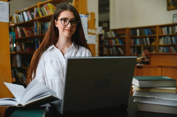 University Library: Beautiful Smart Caucasian Girl uses Laptop, Writes Notes for Paper, Essay, Study for Class Assignment. Focused Students Learning, Studying for College Exams. Side View Portrait.