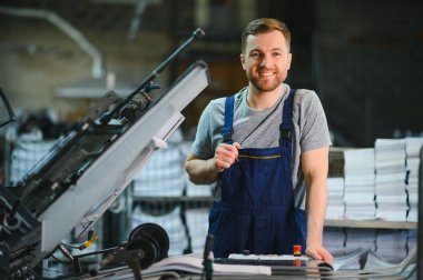 Baskı fabrikasındaki modern ambalaj makinesinin üretim sürecini kontrol eden işçilerin portresi.