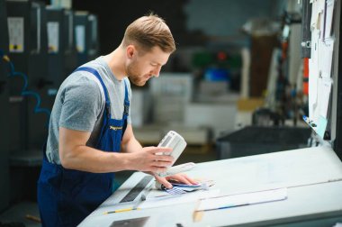Baskı fabrikasındaki modern ambalaj makinesinin üretim sürecini kontrol eden işçilerin portresi.