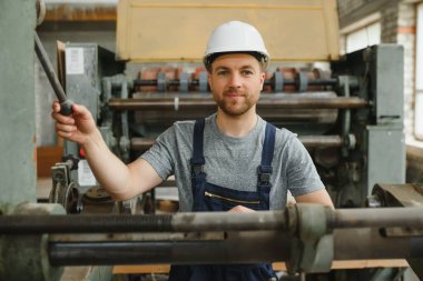 Gülümseyen ve mutlu çalışan. Fabrikada sanayi işçisi. Beyaz şapkalı genç teknisyen.