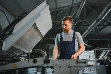 Baskı fabrikasındaki modern ambalaj makinesinin üretim sürecini kontrol eden işçilerin portresi.