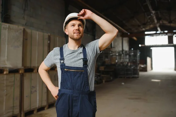 Smiling and happy employee. Industrial worker indoors in factory. Young technician with white hard hat