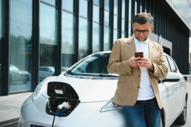 Bir işadamı elektrikli bir arabayı şarj eder.