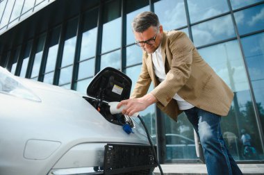 Elektrikli otomobil için güç konektörü tutan adam.