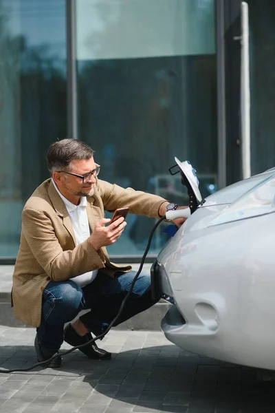 Ein Bärtiger Mann Sitzt Neben Seinem Neuen Modernen Elektroauto Und — Stockfoto