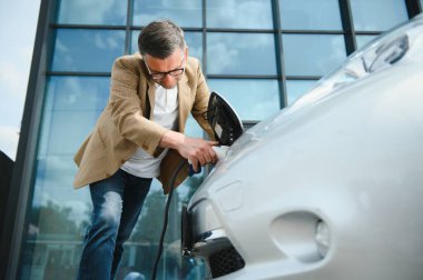 Elektrikli otomobil için güç konektörü tutan adam.