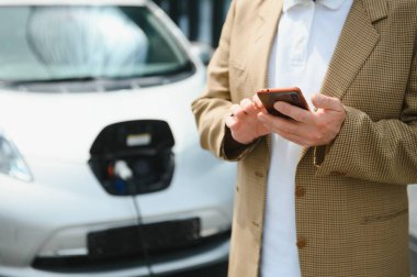 Araba şarj edilirken telefonu kullanan yakışıklı bir adam..