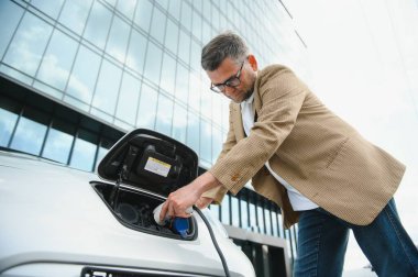 Bir işadamı elektrikli bir arabayı şarj eder.