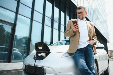Bir işadamı elektrikli bir arabayı şarj eder.