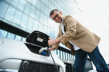 Elektrikli otomobil için güç konektörü tutan adam.