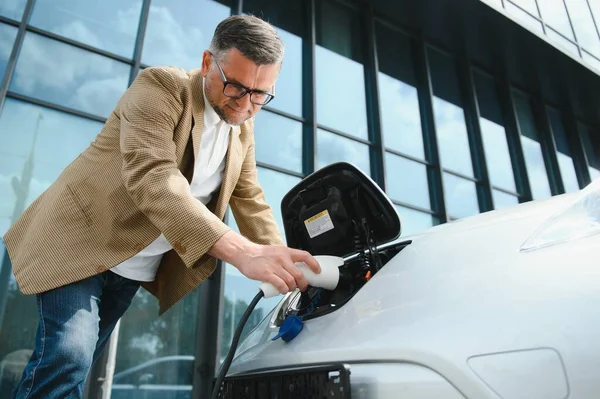 Bir işadamı elektrikli bir arabayı şarj eder.
