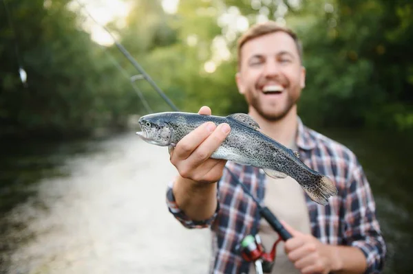 Fly-fisherman holding trout out of the water.