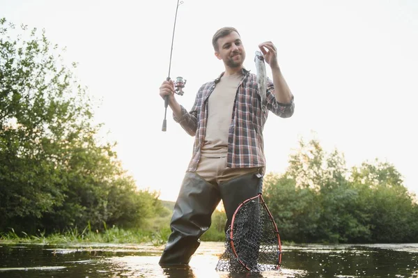 Fly-fisherman holding trout out of the water.