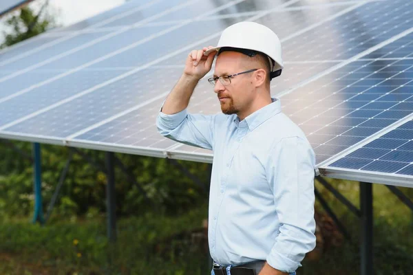 Portrait of male engineer with tablet in his hands near the solar panels station, wearing helmet at sunny day. Green ecological power energy generation
