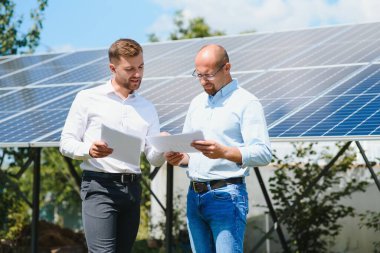 Yenilenebilir enerji anlaşması tamamlandıktan sonra güneş paneline karşı el sıkışan iki kişi.