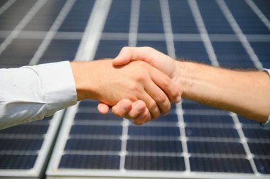 Yenilenebilir enerji anlaşması tamamlandıktan sonra güneş paneline karşı el sıkışan iki kişi.
