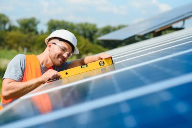 Güneş pili olan bir erkek işçi. Koruyucu kasklı bir adam. Tek başına güneş paneli sistemi kuruluyor.