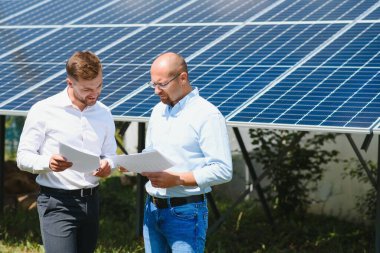 Yenilenebilir enerji anlaşması tamamlandıktan sonra güneş paneline karşı el sıkışan iki kişi.