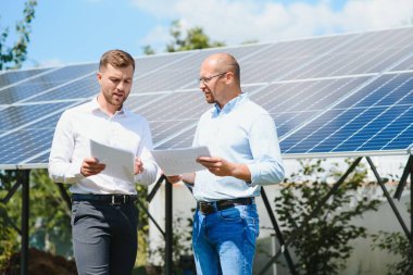 Güneş çiftliği (güneş paneli), iki mühendis ile birlikte sistemin işleyişini kontrol etmek için yürür, dünyanın enerjisini korumak için alternatif enerji, temiz enerji üretimi için fotovoltaik modül fikri.