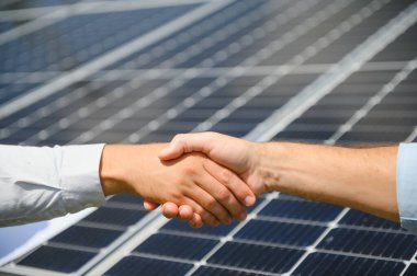 Yenilenebilir enerji anlaşması tamamlandıktan sonra güneş paneline karşı el sıkışan iki kişi.