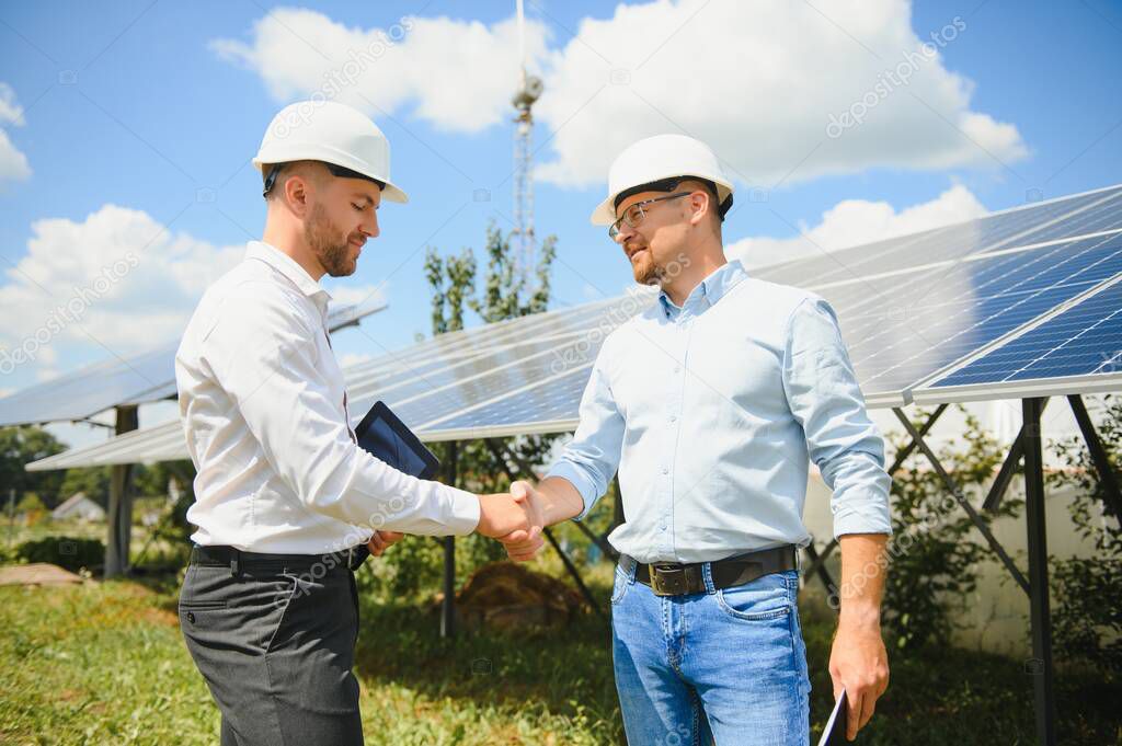 Workers shaking hands on a background of solar panels on solar power plant.
