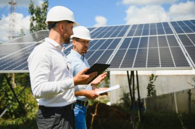 Güneş çiftliği (güneş paneli), iki mühendis ile birlikte sistemin işleyişini kontrol etmek için yürür, dünyanın enerjisini korumak için alternatif enerji, temiz enerji üretimi için fotovoltaik modül fikri.